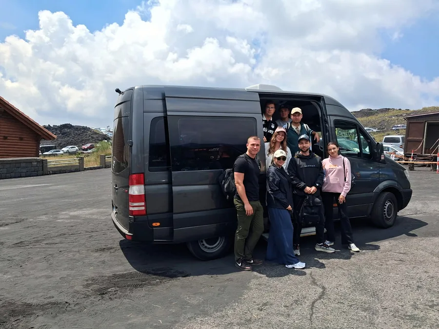 Eine Gruppe junger Leute vor dem geöffneten Sprinter, auf einem Platz am Etna