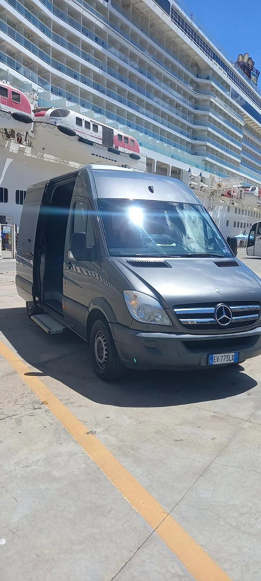 Lo Sprinter grigio scuro in porto, davanti a una nave da crociera, con la porta laterale aperta