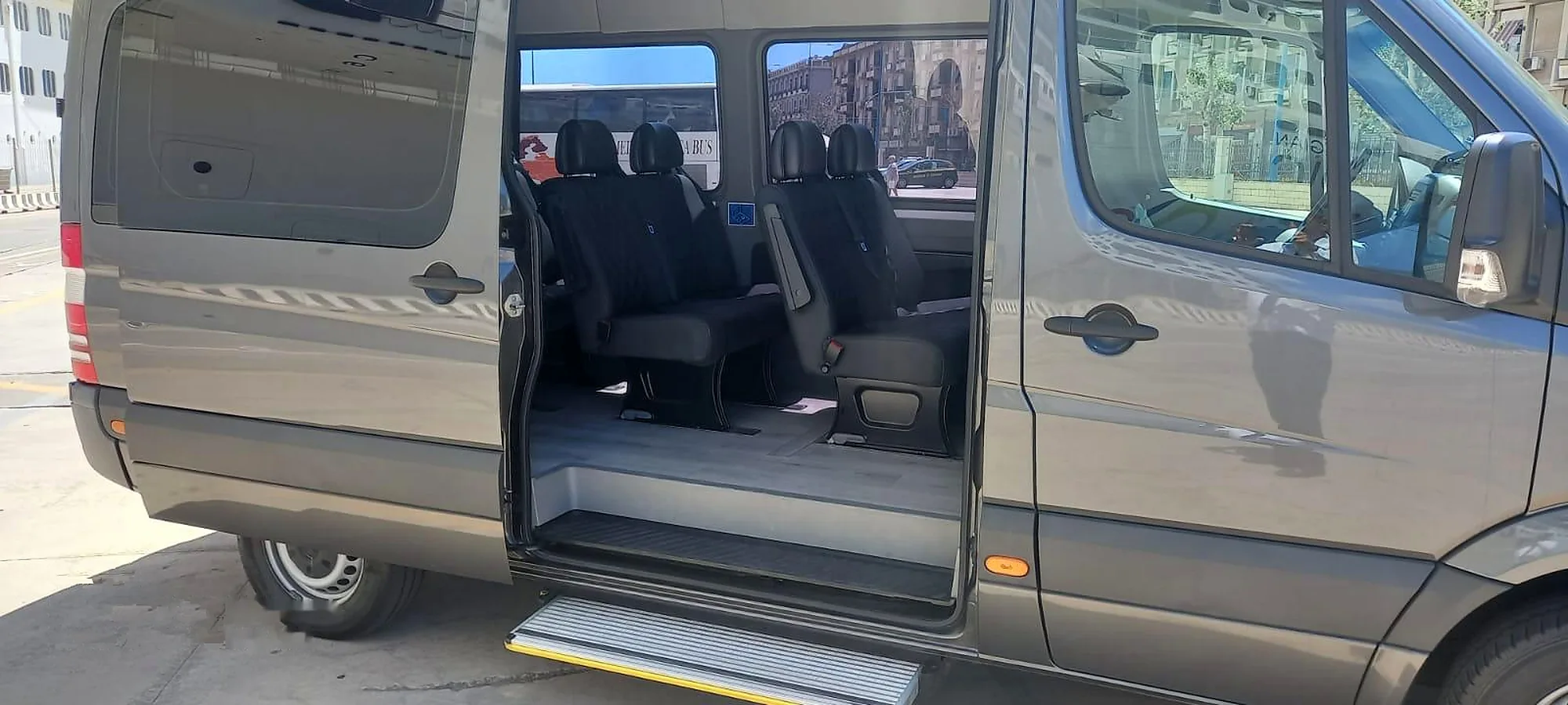 Lo Sprinter grigio scuro con la porta laterale aperta: le file di sedili in pelle e la pedana di accesso