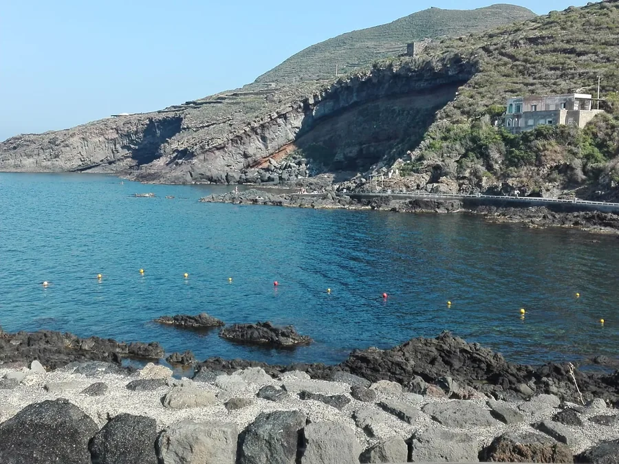 Una bahía de roca volcánica con el mar azul y una casa en la colina