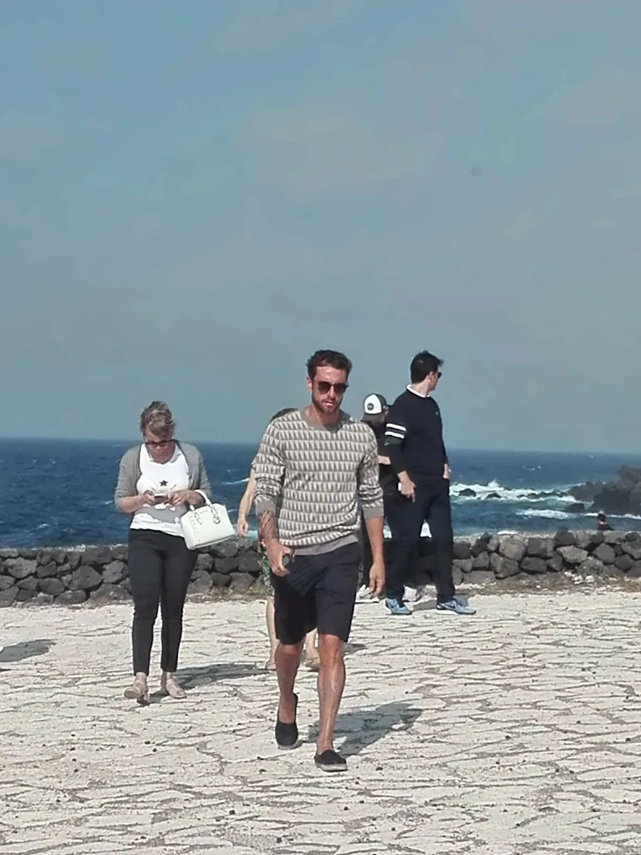 Un invitado camina por una explanada de piedra volcánica, con el mar detrás
