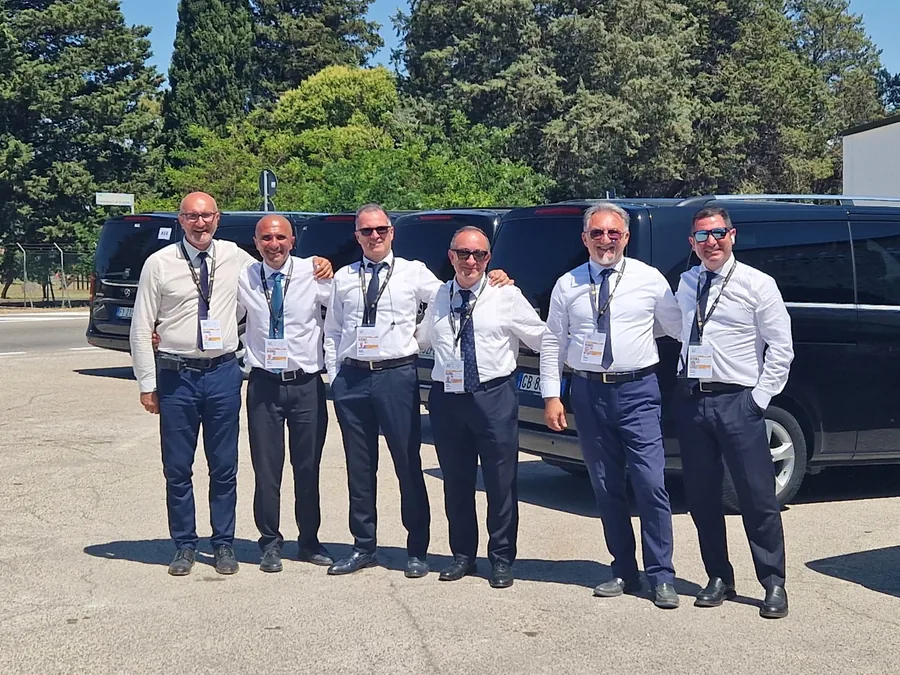 Seis chóferes con camisa blanca y corbata, con el pase de la cumbre, delante de los coches negros