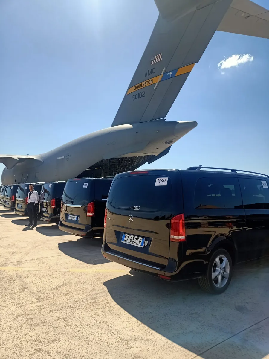 Una fila di auto nere di servizio sotto la coda di un aereo da trasporto, su una pista