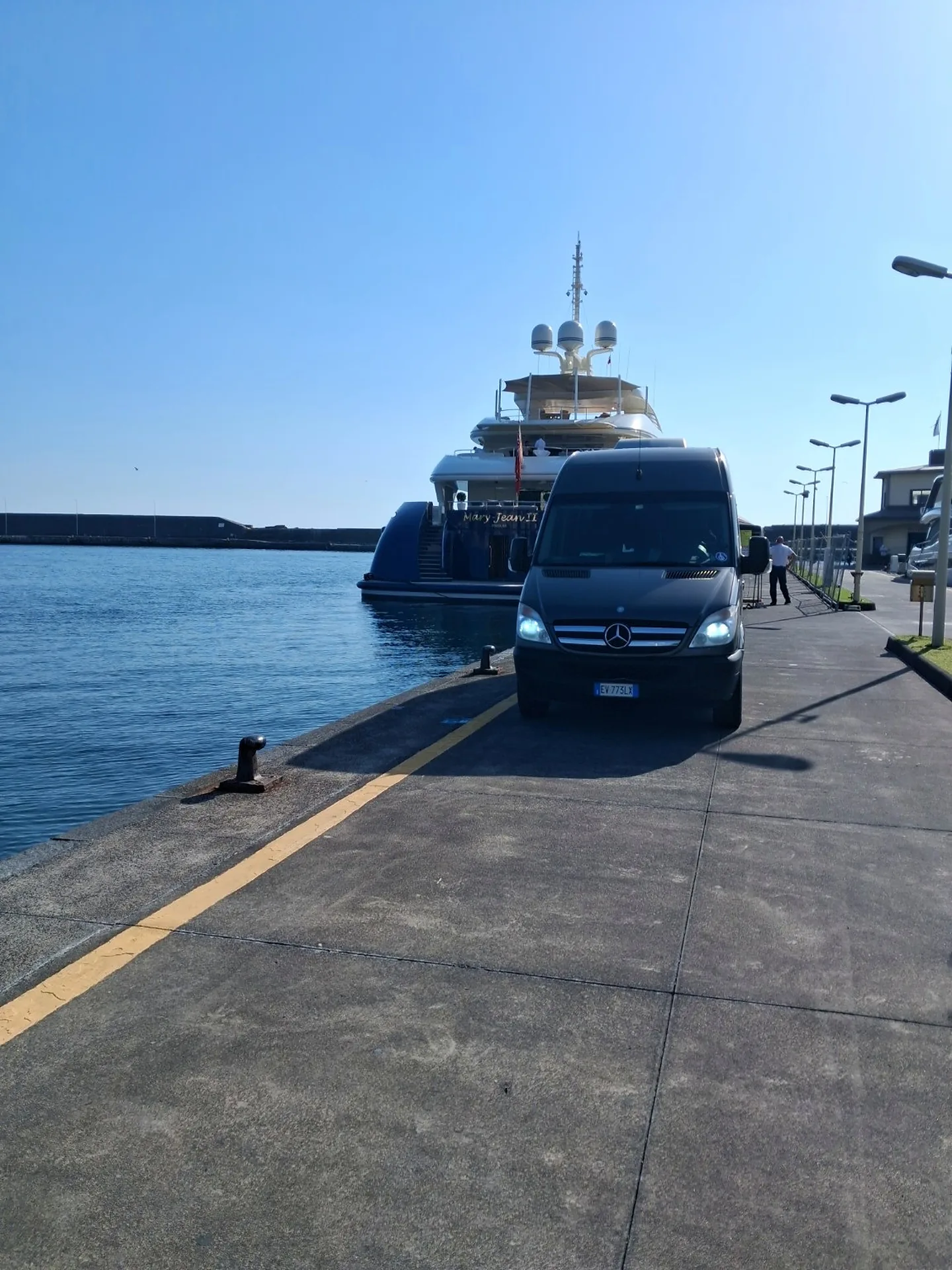 Lo Sprinter grigio scuro di Exclusive Journeys in banchina, con uno yacht ormeggiato alle spalle