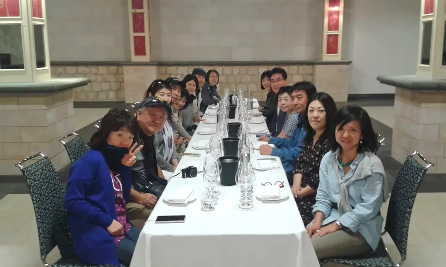 Eine Gruppe von Gästen an einer langen, mit Weingläsern gedeckten Tafel in einem Saal aus Stein
