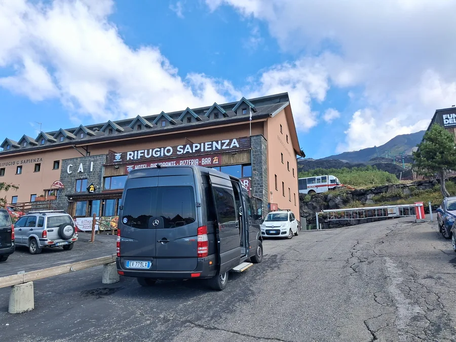 La Sprinter gris oscuro vista desde atrás, con la puerta lateral abierta y el estribo, delante del Rifugio Sapienza en el Etna