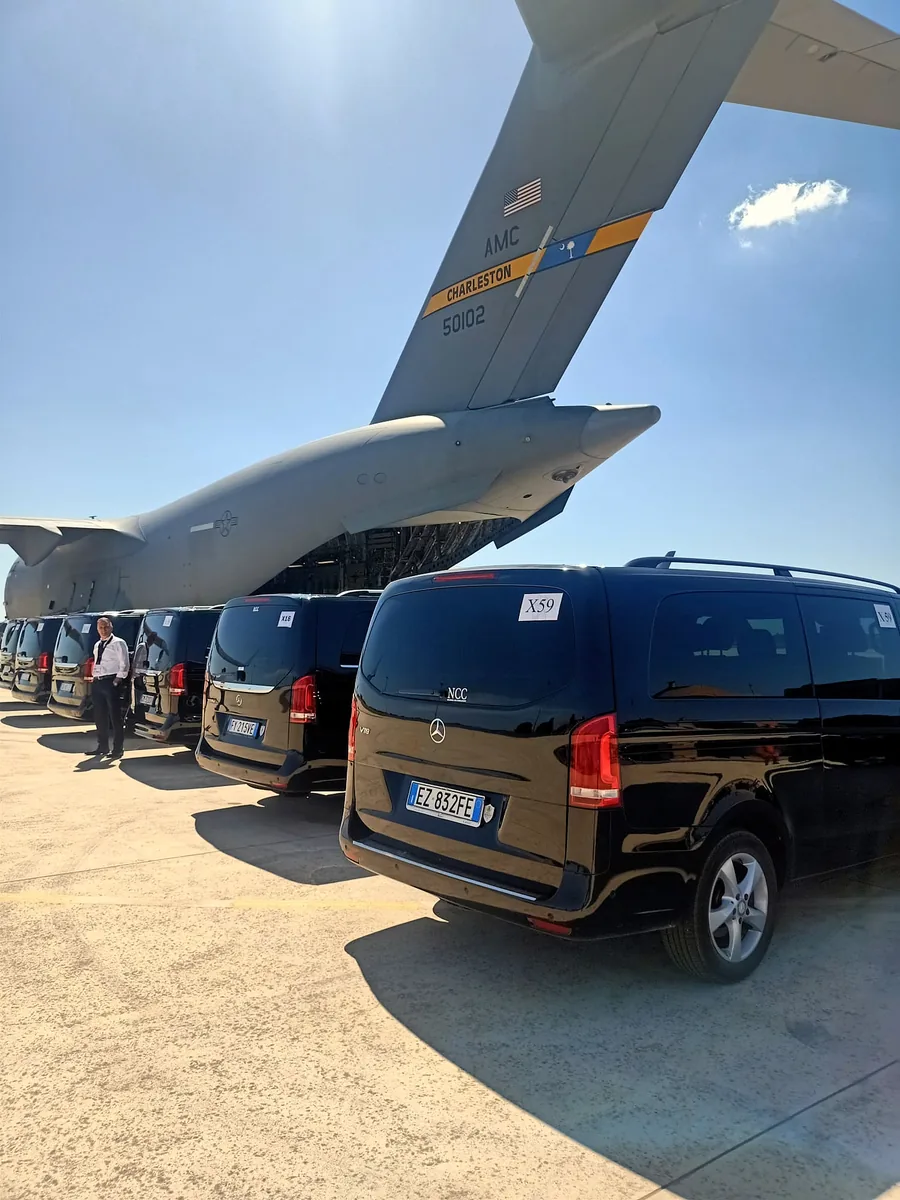 Una fila de coches negros de servicio bajo la cola de un avión de transporte, en una pista