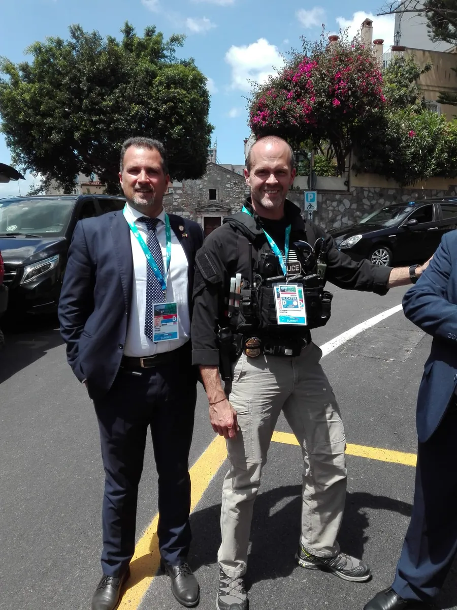 Un autista in abito scuro con il pass del G7, accanto a un agente in divisa, a Taormina